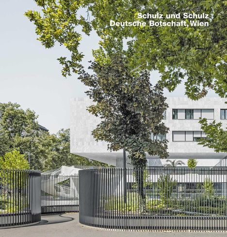 "Schulz und Schulz, Deutsche Botschaft, Wien." Moderne Architektur mit großem weißen Gebäude, umgeben von Bäumen und Zaun.