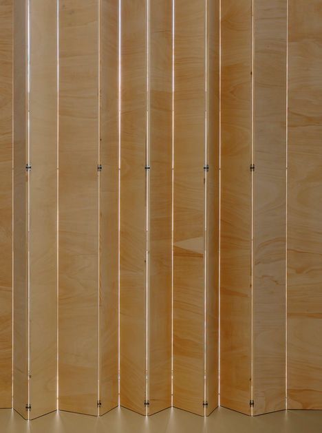 Holzpaneele in einer Reihe, verbunden durch Scharniere. Sie erzeugen ein geometrisches, wellenförmiges Muster.