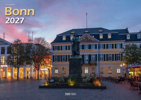 „Bonn 2027“ und „Postamt“ sind zu lesen. Im Vordergrund steht eine Statue auf einem Platz vor einem beleuchteten Gebäude.