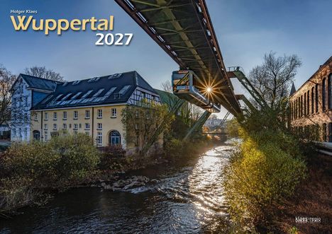 "Wuppertal 2027" steht groß im Bild. Eine Schwebebahn fährt über einen Fluss, daneben alte Gebäude und Bäume im Herbst.
