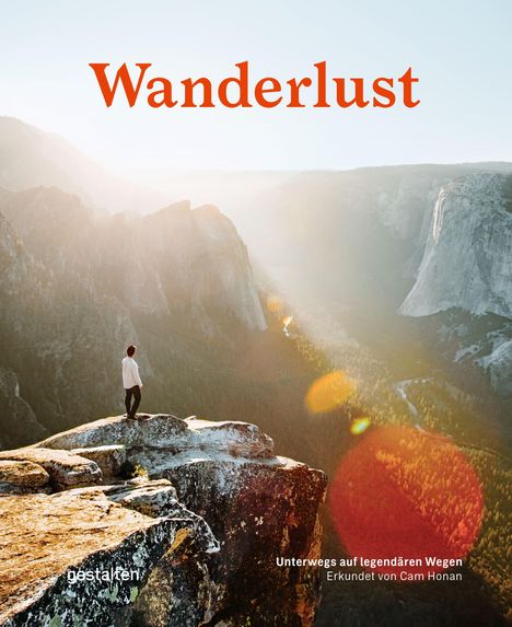 „Wanderlust“ in roter Schrift. Darunter Berge im Sonnenlicht mit einer Person auf einem Felsvorsprung.