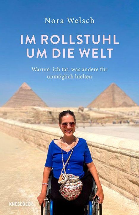 Titel: "Im Rollstuhl um die Welt". Eine Frau im Rollstuhl vor Pyramiden in der Wüste. Sie lächelt und trägt eine Sonnenbrille.