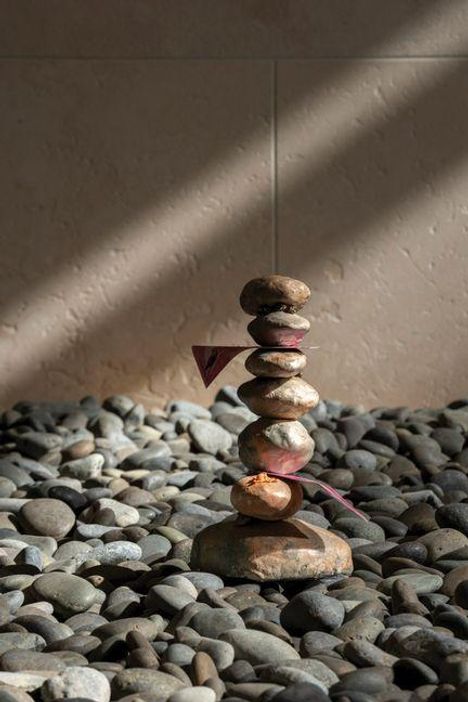 Keine erkennbaren Texte. Ein Steinhaufen auf Kieseln, durchdrungen von Sonnenlicht, in einem ruhigen Raum arrangiert.