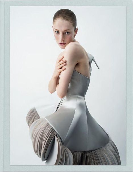 Eine Frau in einem avantgardistischen, grauen Kleid mit voluminösem Rock und Korsett-Oberteil, posiert elegant.