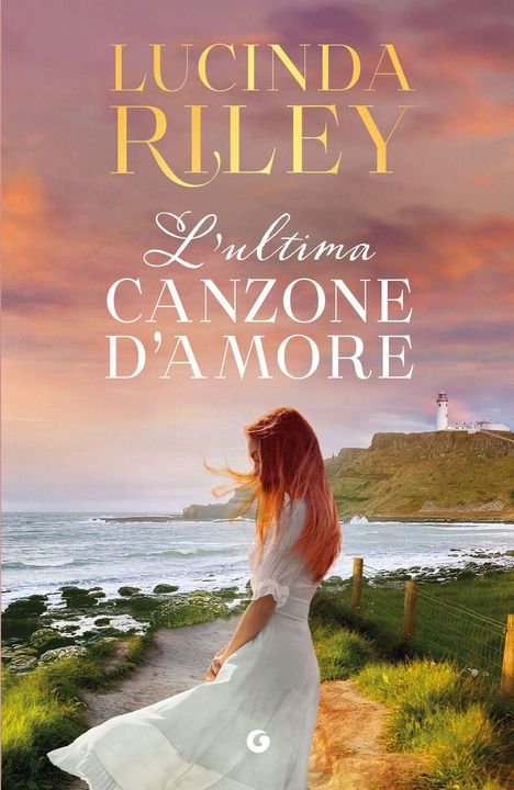 Titel: "L'ultima Canzone D’Amore" von Lucinda Riley. Eine Frau in weißem Kleid am Meer bei Sonnenuntergang mit einem Leuchtturm.