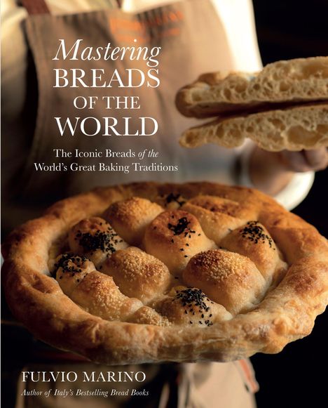 Text: Mastering Breads of the World. Grobes Brot mit schwarzem Sesam und hellbrauner Kruste, Person im Hintergrund.