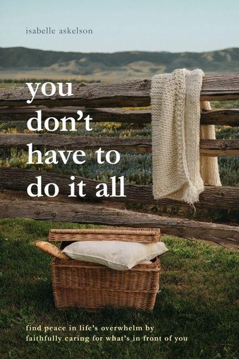 „You don’t have to do it all.“ Ein Korb mit Decke vor einem Holzzaun in ländlicher Landschaft.
