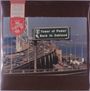 Ein Straßenschild zeigt „Tower of Power Back to Oakland“. Darunter eine befahrene Brücke über Wasser in einer urbanen Umgebung.