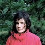 Ich weiß nicht, wer das ist. Eine Person in roter Jacke steht vor Nadelbaum, schaut direkt in die Kamera.