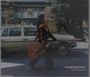 Text: "svegliaginevra" und "la fine della guerra". Eine Person trägt eine Gitarre vor einem altmodischen Auto.