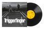 "Triggerfinger" in großen Buchstaben. Zwei Männer im Anzug auf einer Straße, im Hintergrund eine Stadtansicht.