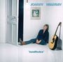 "JOHNNY HALLYDAY" und "insolitudes" stehen in blauer Schrift. Ein Mann sitzt lächelnd am Boden neben einer Akustikgitarre.
