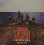 „MAN OF THE NORTH, LIVE IN THE WILD, LIAM ST. JOHN.“ Eine Band steht auf einer Klippe am Meer.