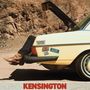 Texte: "Kensington Edition", "Plaza", "Stereo Sound". Beine in Cowboystiefeln ragen aus dem Kofferraum eines gelben Autos.