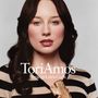 "Tori Amos Strange Little Girls." Eine Frau mit dunklem Haar trägt ein gestreiftes Oberteil, hält eine goldene Pistole.