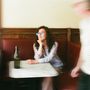 Unschärfe zeigt Person mit blauer Brille an Marmortisch, leere Flasche, rote Sitzbank, verwischter Passant.