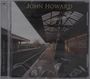 Texte: "JOHN HOWARD", "OVERNIGHT BAGS", "THINK LIKE A KEY MOD SERIES". Eine Person steht auf einem Gleis unter einem überdachten Bahnsteig.