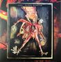 Text: "COIL · ASTRAL DISASTER". 

Eine abstrakte Figur mit mehreren Armen und maskenartigem Gesicht vor feurigem Hintergrund.