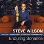 "STEVE WILSON", "Enduring Sonance". Ein Mann sitzt mit Saxophon auf einem orangefarbenen Sofa vor einem geometrischen Wandmuster.