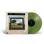 "THE JAYHAWKS" oben auf einem Plattencover. Darunter "Sanctuary Park". Grünes Vinyl daneben. Landschaft im Rahmen.