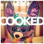 Oben "OREN AMBARCHI", groß "COOKED", unten "DC994". Darunter eine bunte, glitzernde Plüschfigur.