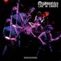 „Mephistofeles: Live in Europe, Stereo Recording.“ Dunkle Bühne, Musiker mit Gitarren und Schlagzeug. Dynamische Lichtstimmung.