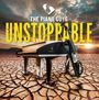 "The Piano Guys, Unstoppable" in großen Buchstaben über einem Piano und Cello auf trockener, rissiger Erde bei Sonnenuntergang.