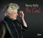 Text: "Nancy Kelly Be Cool." Porträt einer lächelnden Frau mit blondem Haar vor dunklem Hintergrund.