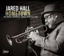 "Jared Hall Hometown" mit Musikernamen. Ein Mann spielt Trompete, trägt Hut und Brille, im Hintergrund Ziegelwand.
