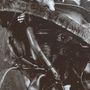 Zerquetschtes Metall, darunter zwei gemalte Augen, alles in sepia gehalten, wirkt rostig und abgenutzt.