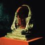 Eine dunkle, atmosphärische Skulptur, die wie ein geöffneter, organischer Torbogen mit angedeuteten Zähnen aussieht, auf einem Sockel.