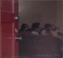 "Hot Mulligan - Pilot" steht unten. Eine rote Tür ist halb geöffnet, im Hintergrund unscharf sitzende Menschen auf einem Sofa.