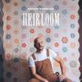 Text: "NATHAN EVANS FOX HEIRLOOM". Ein Mann sitzt vor einer bunten Patchwork-Decke, trägt Brille und braune Latzhose.
