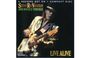 "2-RECORD SET ON 1 COMPACT DISC" und "STEVIE RAY VAUGHAN AND DOUBLE TROUBLE LIVE ALIVE" in goldener und grüner Schrift. Ein Musiker spielt Gitarre, trägt einen Hut und eine glänzende Jacke.