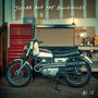 „Josiah and the Bonnevilles“ und „As Is“. Eine alte Motorrad in einer Werkstatt steht neben einem roten Werkzeugschrank.