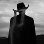 "DEVON GILFILLIAN" und "TIME WILL TELL" oben. Silhouette eines Mannes im Anzug mit Cowboyhut, aus dem Sand fließt. Schwarz-weiß.