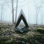 Eine moderne Skulptur mit dreieckiger Öffnung steht in nebligem Wald auf moosbedecktem Boden.