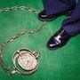 Ein Mann in eleganten schwarzen Schuhen steht auf grünem Boden, neben einer rostigen Metallfalle mit Kette.