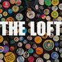 Große, weiße Schrift "THE LOFT" auf einer mit bunten Ansteckbuttons bedeckten Jeansjacke.