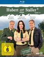 „Hubert ohne Staller“, Staffel 13. FSK 6. Drei Personen in Polizeiuniform vor grauem Berg-Hintergrund.