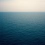 Weite Sicht auf ein ruhiges, blaues Meer unter einem bewölkten Himmel. Keine sichtbaren Texte oder spezifische Details.