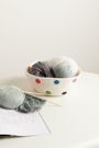 Eine Schale mit bunten Punkten, gefüllt mit Garnknäueln. Davor liegt ein Strickprojekt auf einer Anleitung.