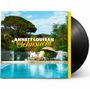 Text: "ANNETT LOUISAN Sehnsucht". Eine Frau sitzt an einem Pool, umgeben von Natur und Liegestühlen.