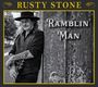 "RUSTY STONE", "RAMBLIN' MAN". Schwarz-Weiß-Foto eines Mannes mit Hut und Gitarre, an eine Wand gelehnt.