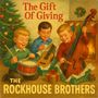"The Gift Of Giving" und "THE ROCKHOUSE BROTHERS". Drei lachende Kinder mit Instrumenten, Weihnachtsbaum rechts.