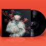 Ein schwarzes Vinyl auf orangefarbenem Hintergrund. Dazu ein unscharfes, abstraktes Cover mit roten Pinselstrichen.