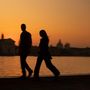 Zwei Personen gehen vor einem Sonnenuntergang, im Hintergrund eine Stadtsilhouette und ein Gewässer.