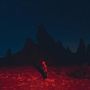 Kein Text sichtbar. Eine rote Landschaft bei Nacht mit einem Skelett im Vordergrund, das auf felsige Spitzen schaut.
