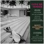 Texte: LOVE ME TENDER, MONTY ALEXANDER TRIO, Titelliste. Frau in weißem Kleid entspannt auf Steinstufen vor modernem Haus mit Palmen.