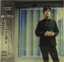 Text: "Johnny Marr", japanische Schriftzeichen. Ein Mann in schwarzem Anzug steht vor einem Streifenhintergrund.